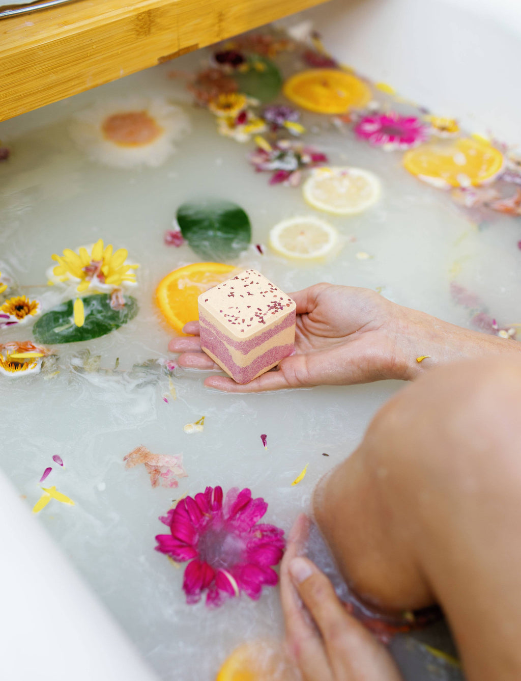 Square bath bomb cube held in hand, pale lavender and pink with small speckles
