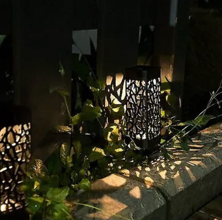 Black solar pathway lantern light with cutout grille, warm glow beside walkway