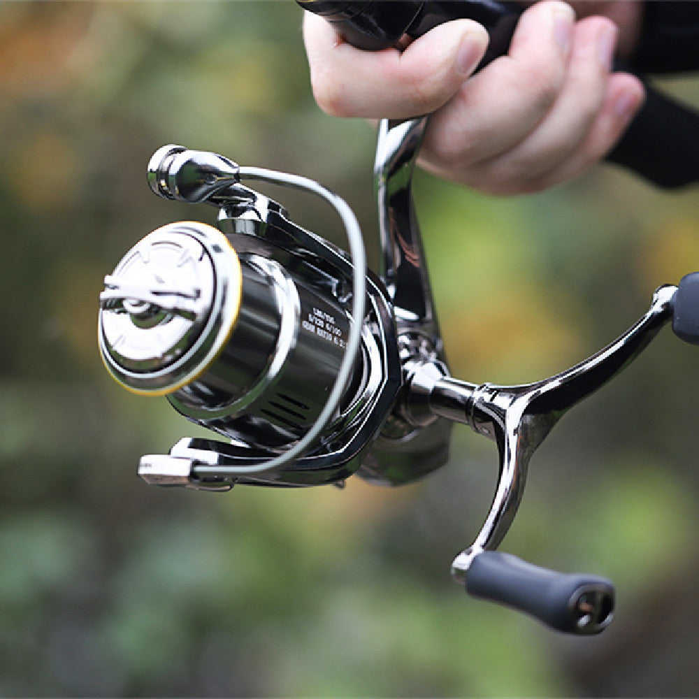 Metal spinning fishing reel with black handle grips and silver spool, held in hand.