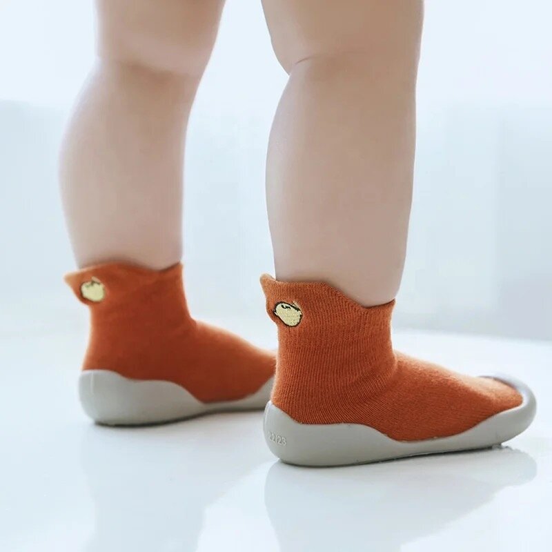 Orange barefoot sock shoes on feet with an embroidered fruit patch and white sole.