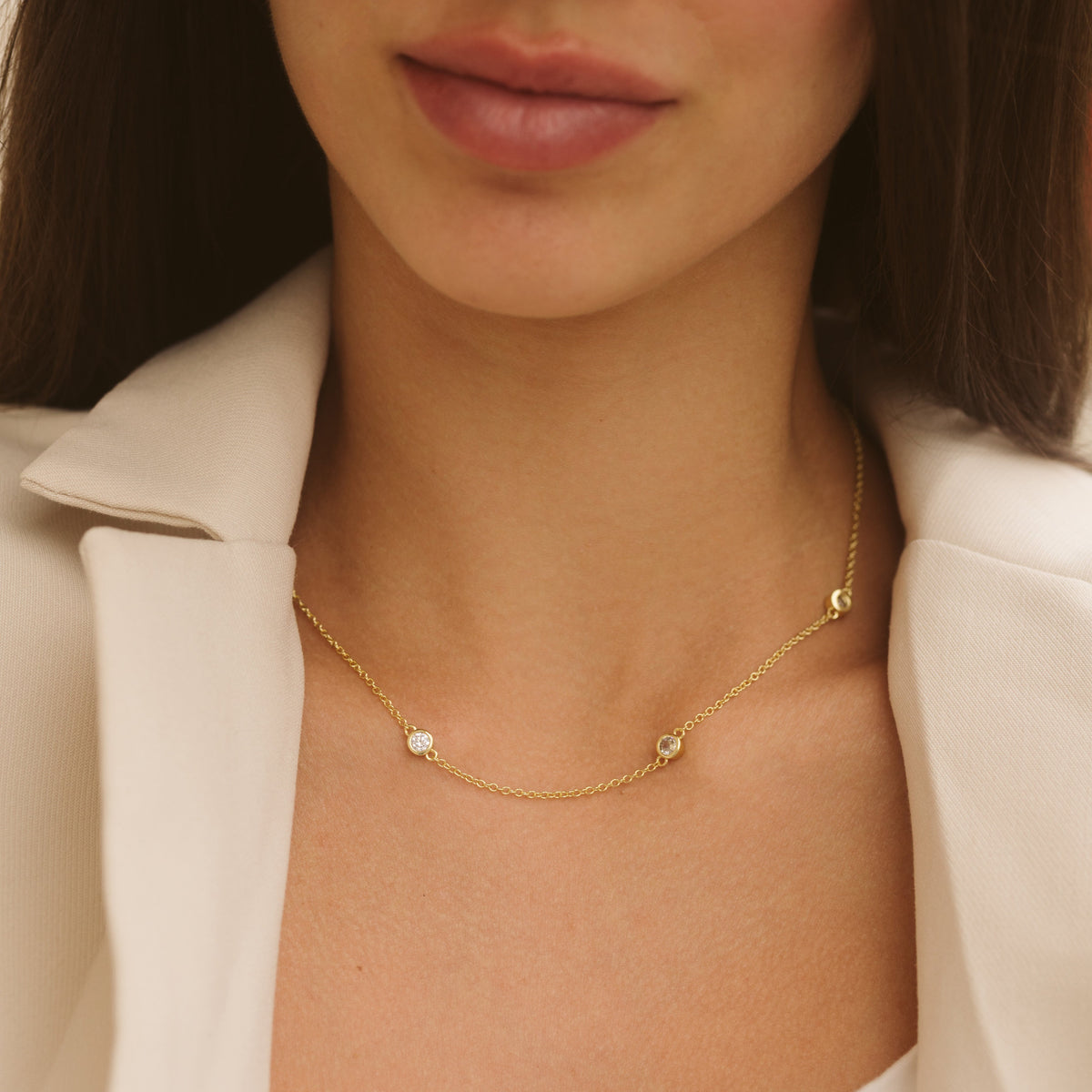 Close-up gold chain necklace featuring five round diamond-like stones