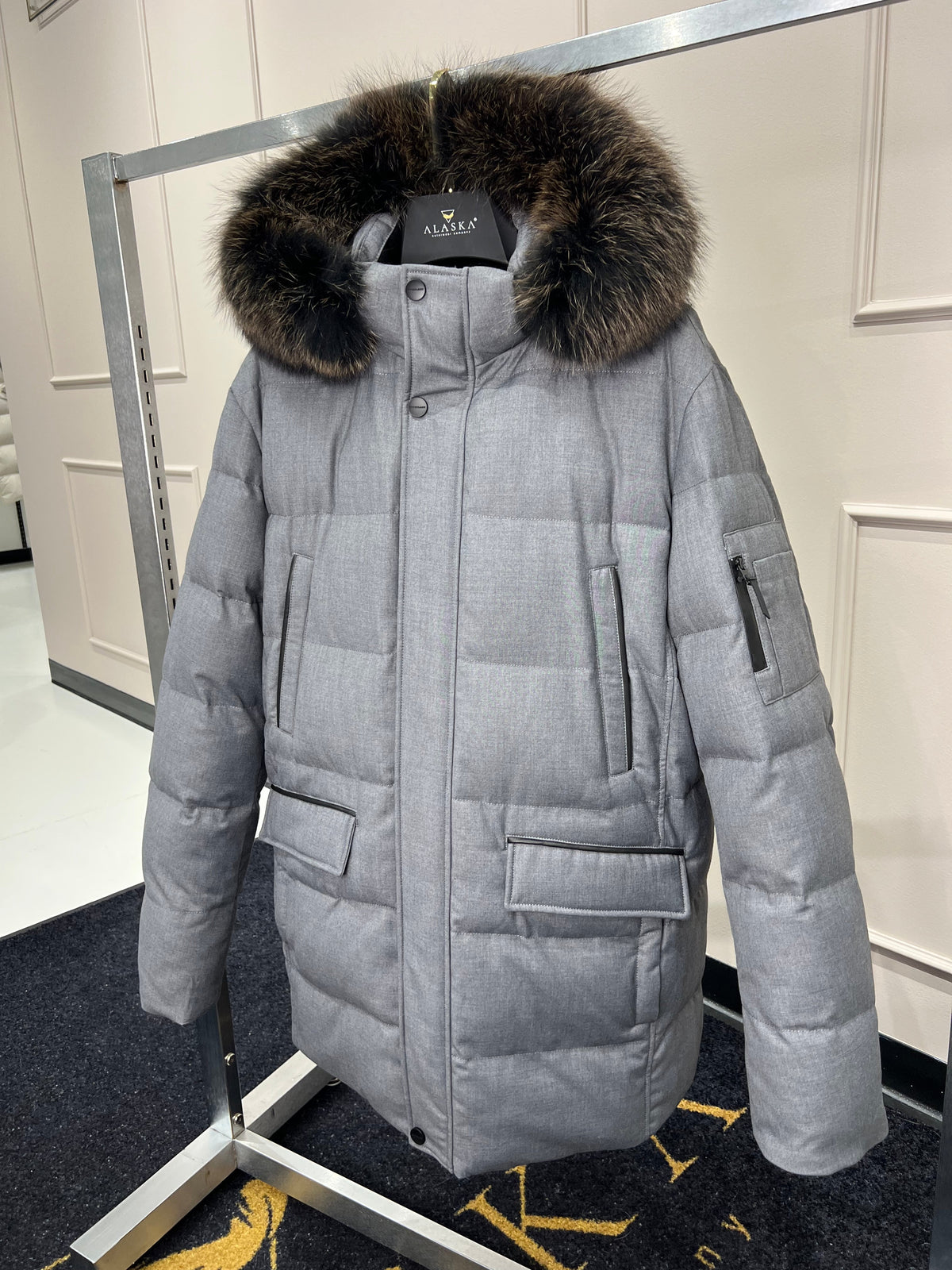 Grey long puffer coat with faux fur hood trim, front zipper, and side pockets