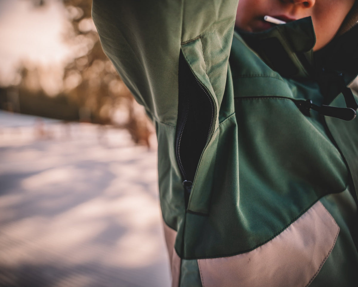 Waterproof snowsuit side close-up with front pocket flap and zipper trim in dark green