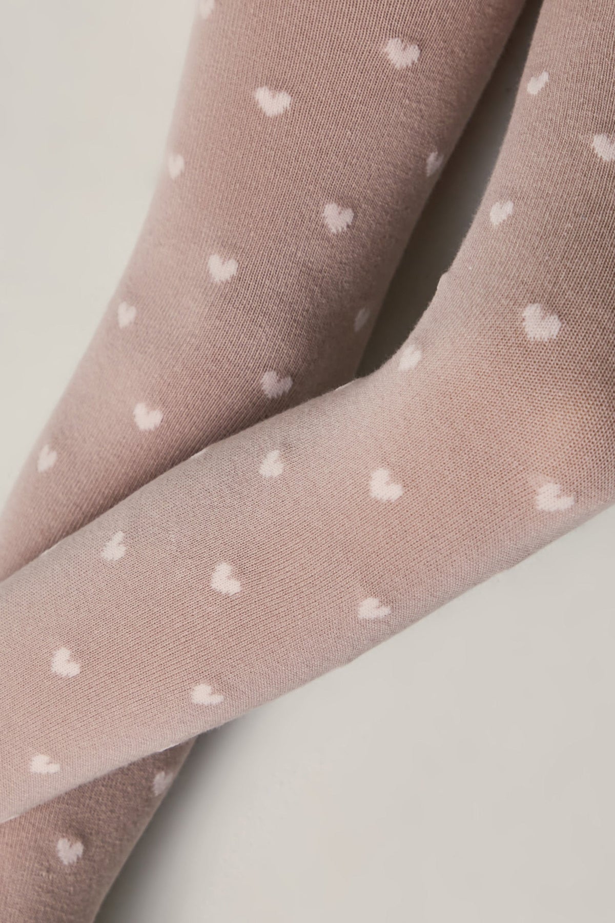 Kids cotton tights in light pink with small white hearts pattern, close-up on leg