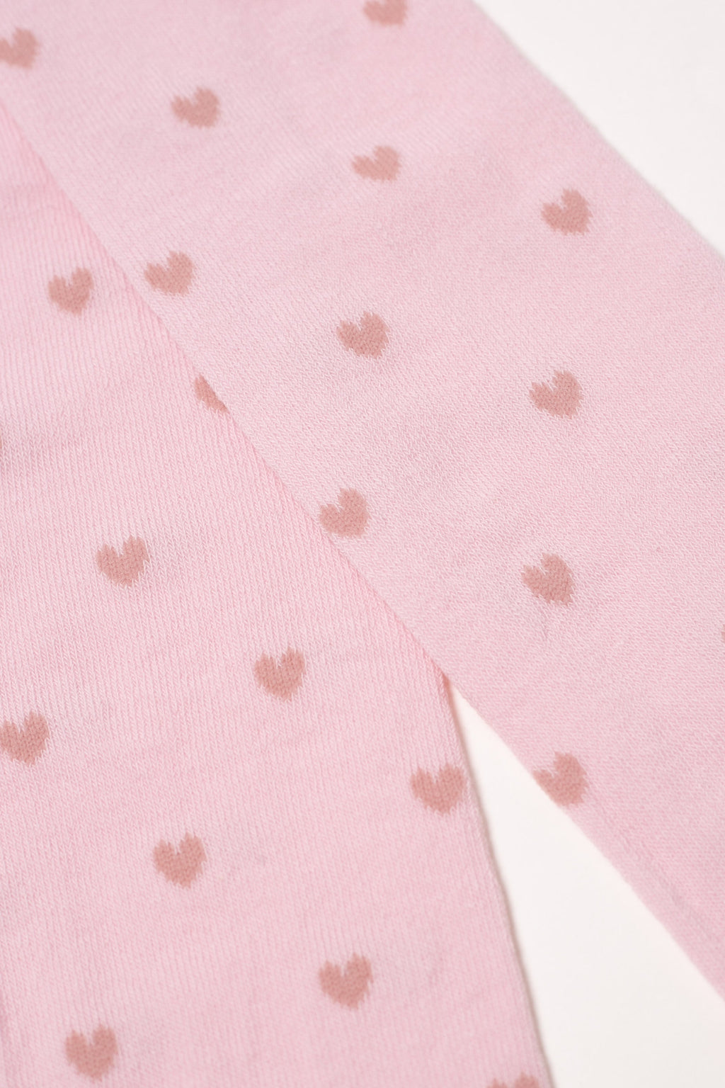 Light pink kids cotton tights with small brown hearts, diagonal fabric close-up