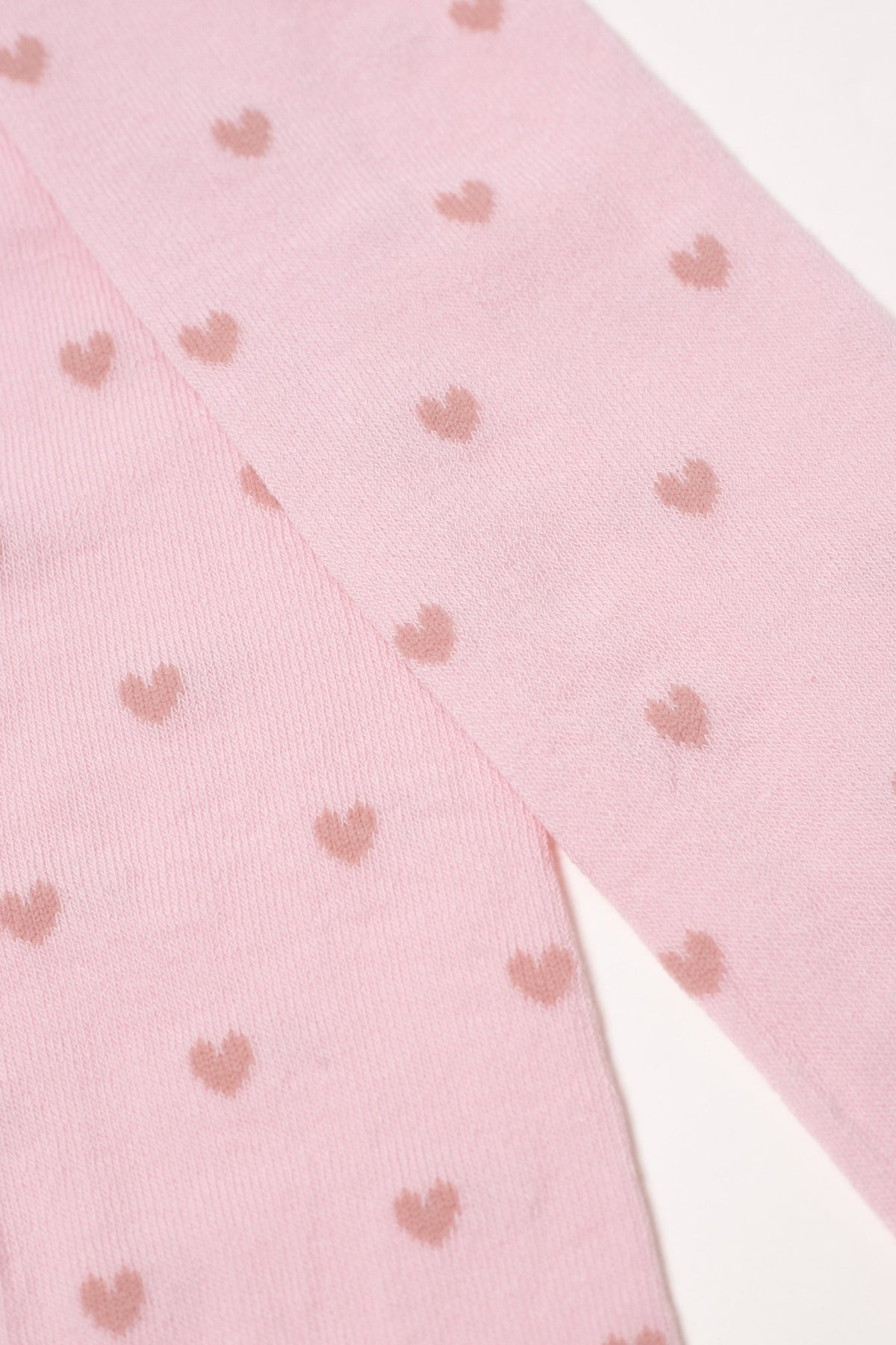 Light pink kids cotton tights with small brown hearts, diagonal fabric close-up