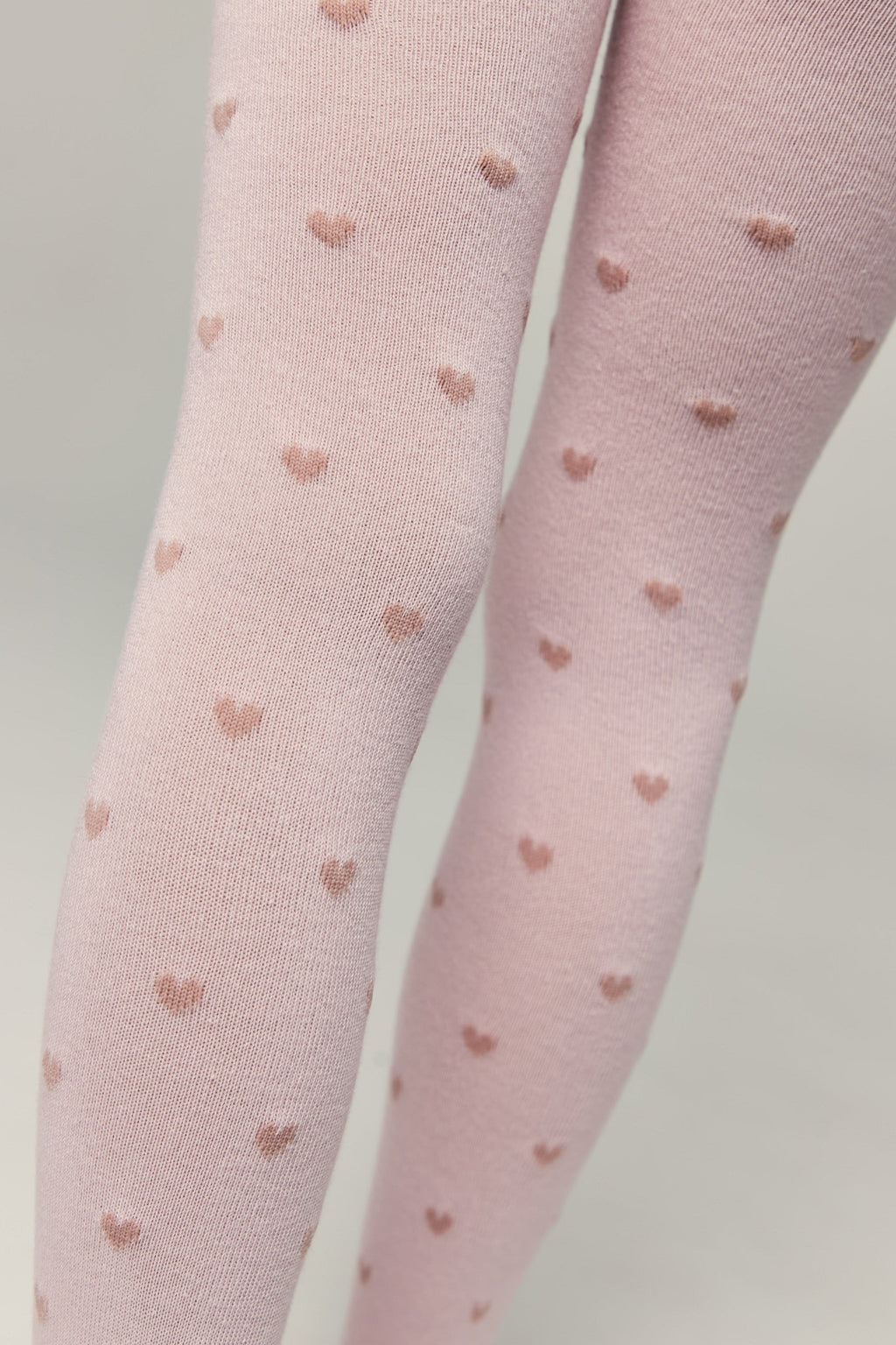 Light pink kids cotton tights with small brown heart pattern, leg close-up