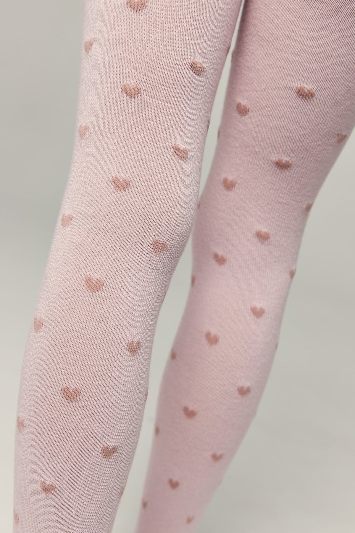 Light pink kids cotton tights with small brown heart pattern, leg close-up