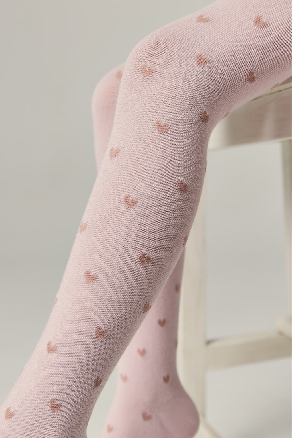 Light pink kids cotton tights with small brown hearts, angled leg and foot