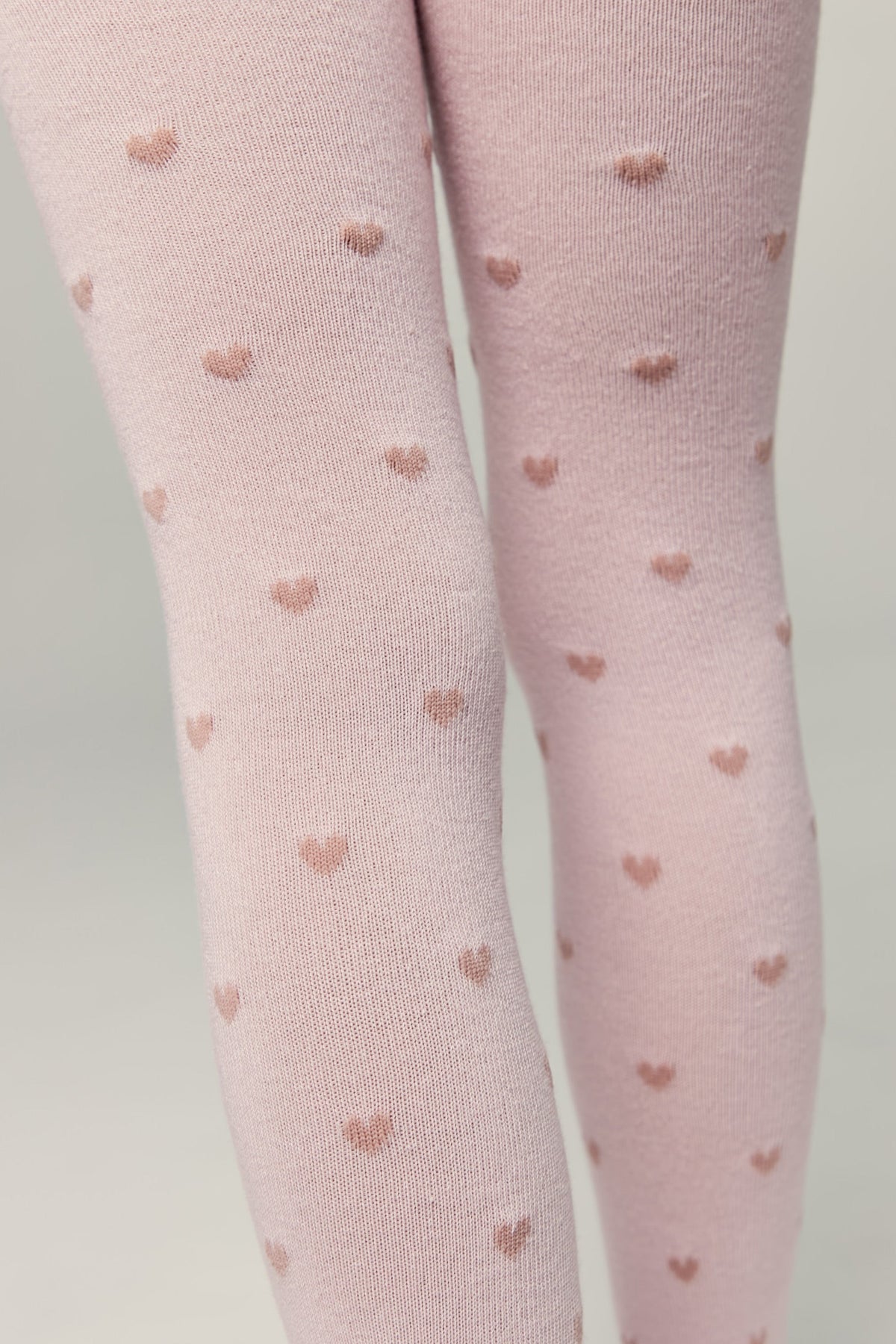 Light pink kids cotton tights with small brown heart pattern, leg close-up