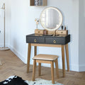 Makeup vanity table set with round illuminated mirror, black drawers, and beige stool