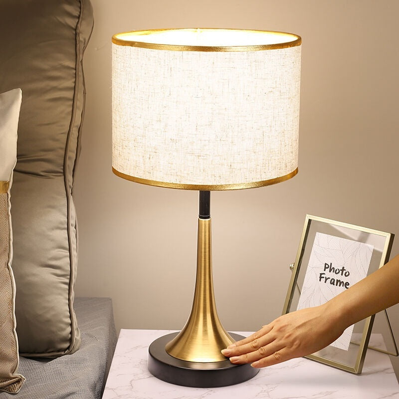 Gold table lamp with off-white fabric shade, dark round foot, and gold column stand