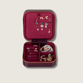 Red velvet travel jewelry box open with gold zipper, compartments, and ring and necklace holders