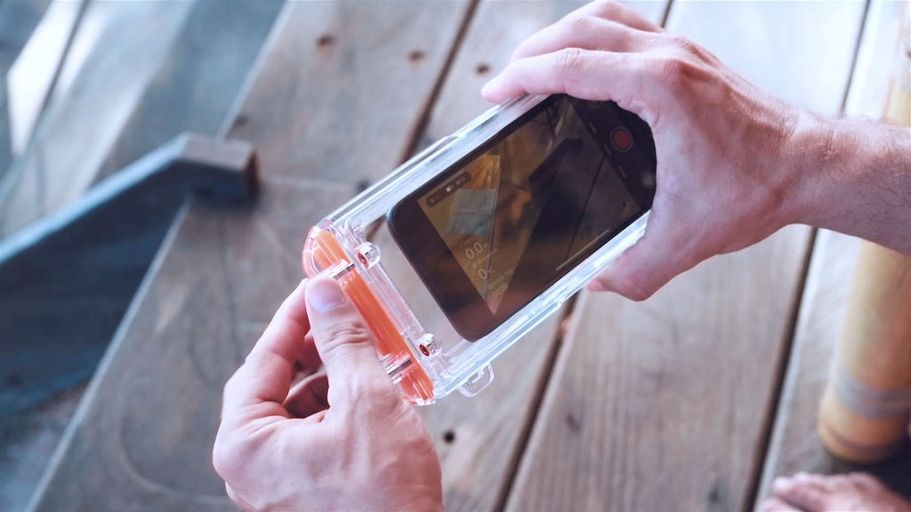 Hands inserting a phone into a clear waterproof phone case with orange latches.
