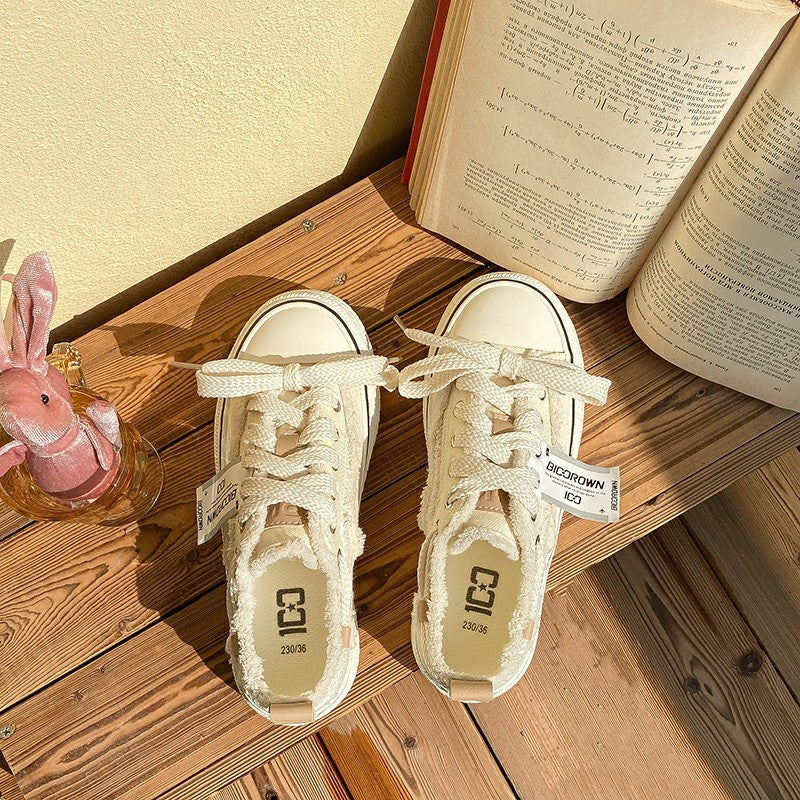 Pair of cream low-top canvas sneakers with white laces and inner logo label.
