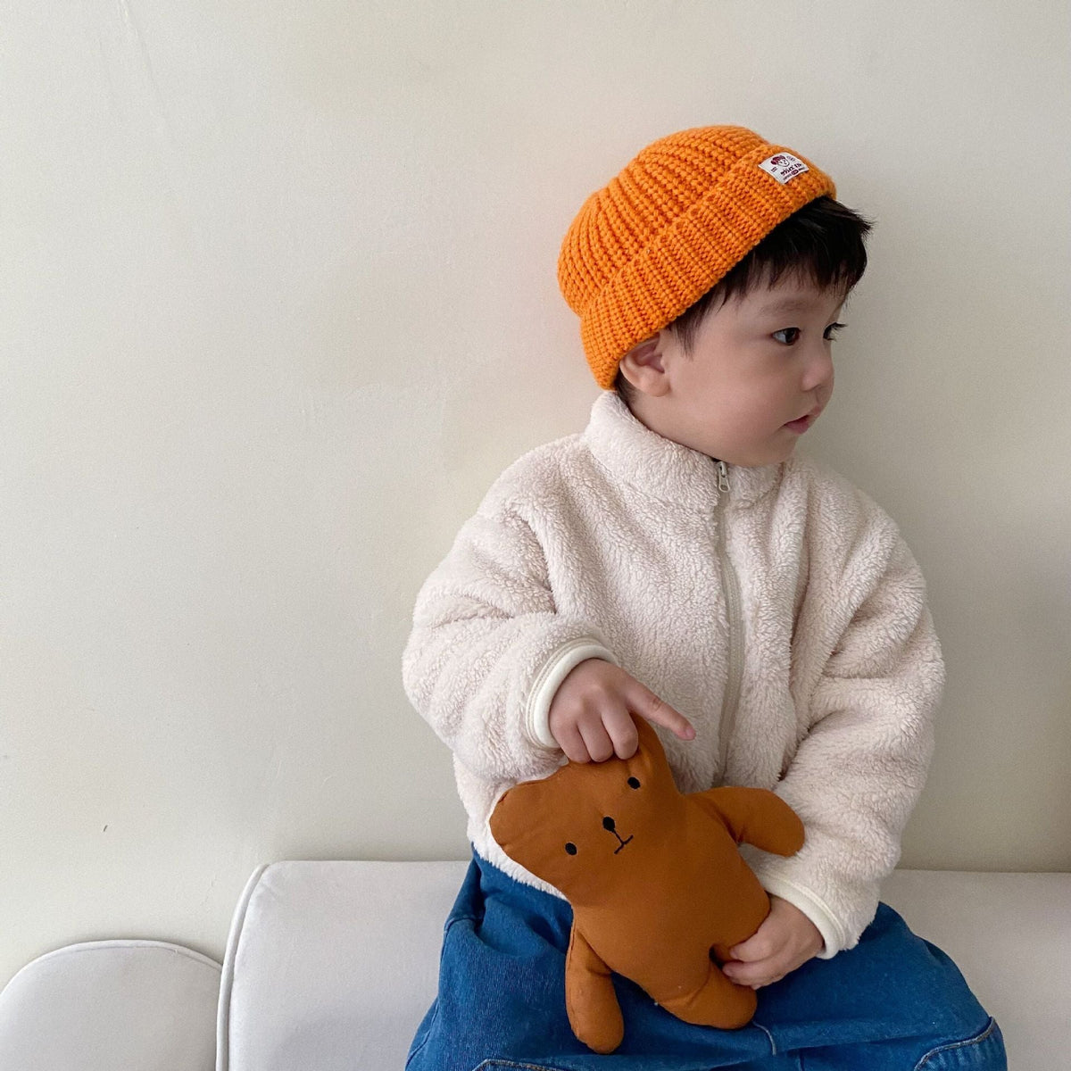 White kids fleece zip jacket with hood, worn with an orange knit beanie.