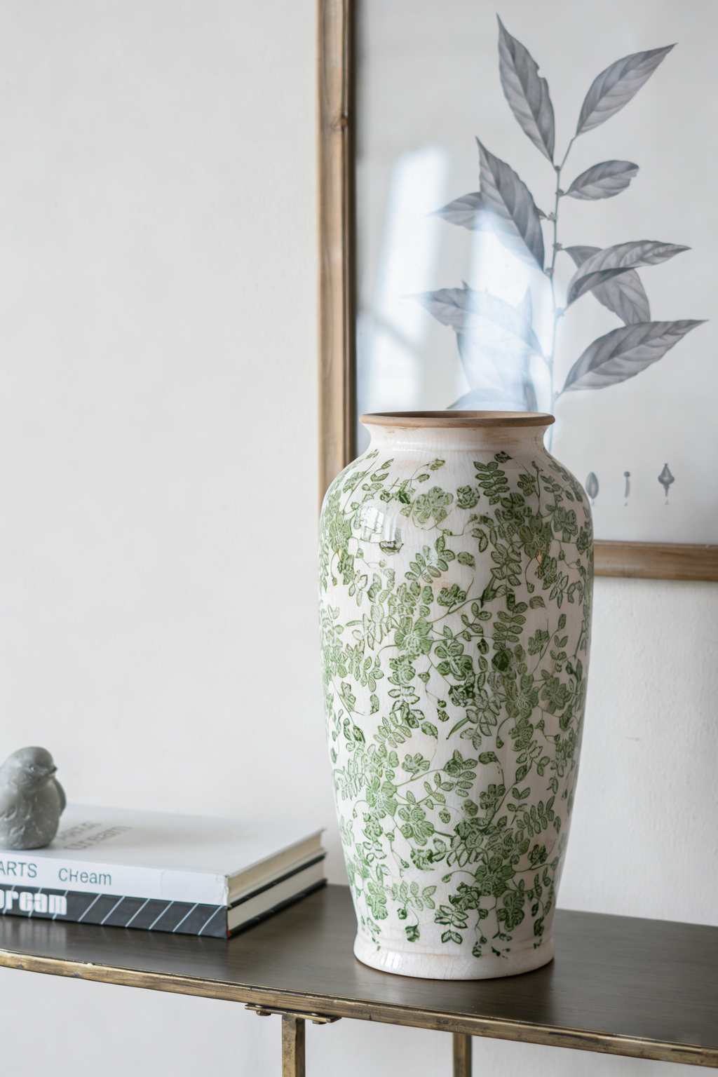 White ceramic vase with green floral leaf pattern standing on a narrow shelf