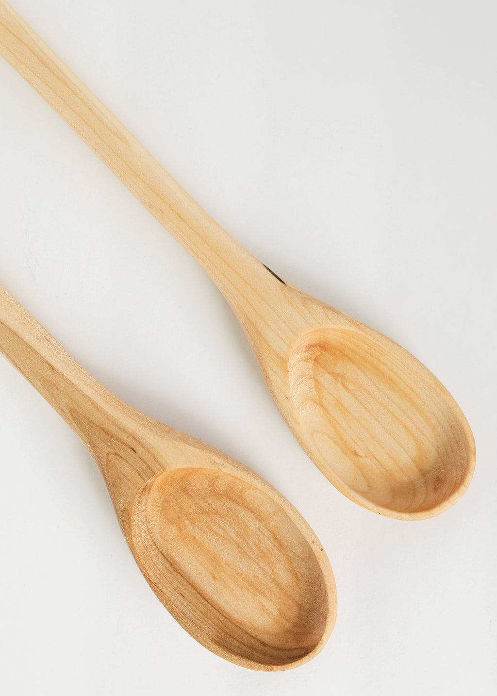 Close-up of two light wood spoons, oval bowls showing visible grain.