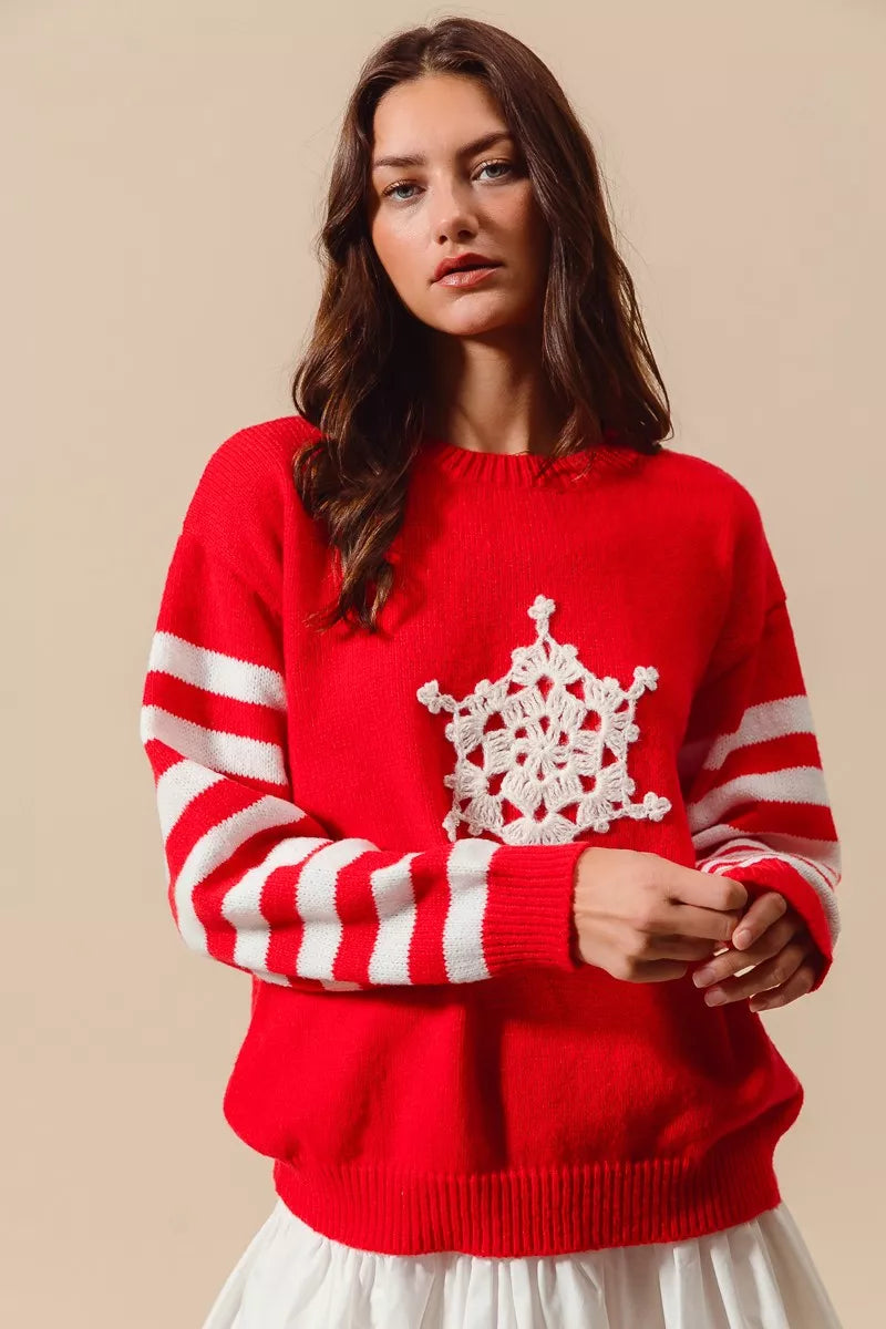 Red knit sweater with white crochet snowflake applique and striped sleeves at cuffs