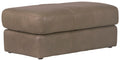 Putty leather ottoman with cushioned top and square base, stitched seams.