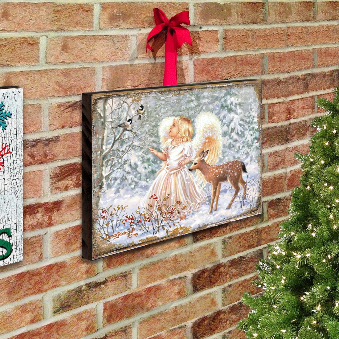 Framed wooden wall art mounted on brick wall with angel and deer in snow