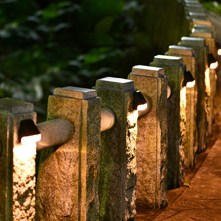 Solar LED wall lamps on stone fence posts, warm light shining from square openings