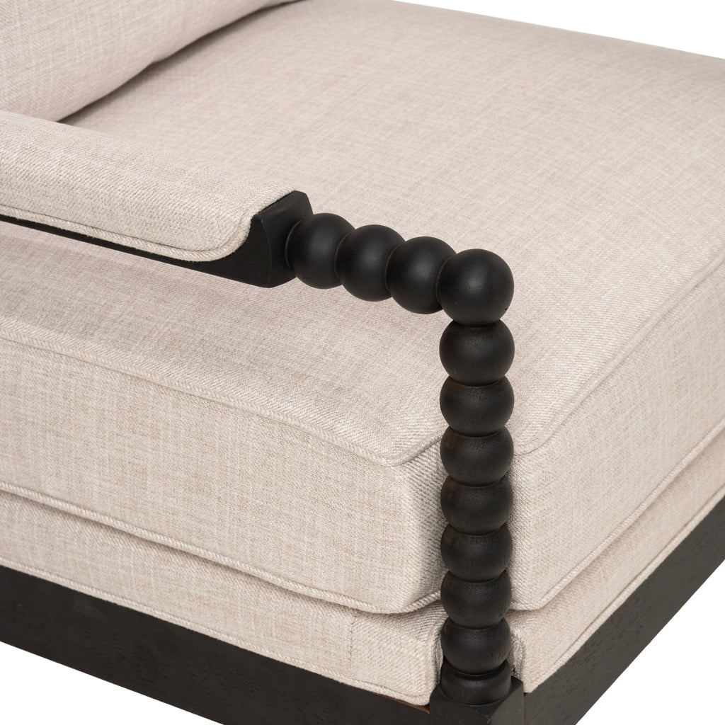 Upholstered accent chair close-up with beige fabric cushions and a dark wood bead-style armrest