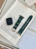 Christmas watch strap with dark green woven fabric and metal clasp, shown on a book