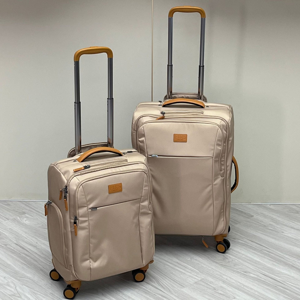 Two cream wheeled trolley suitcases with telescoping handles and orange-trim details