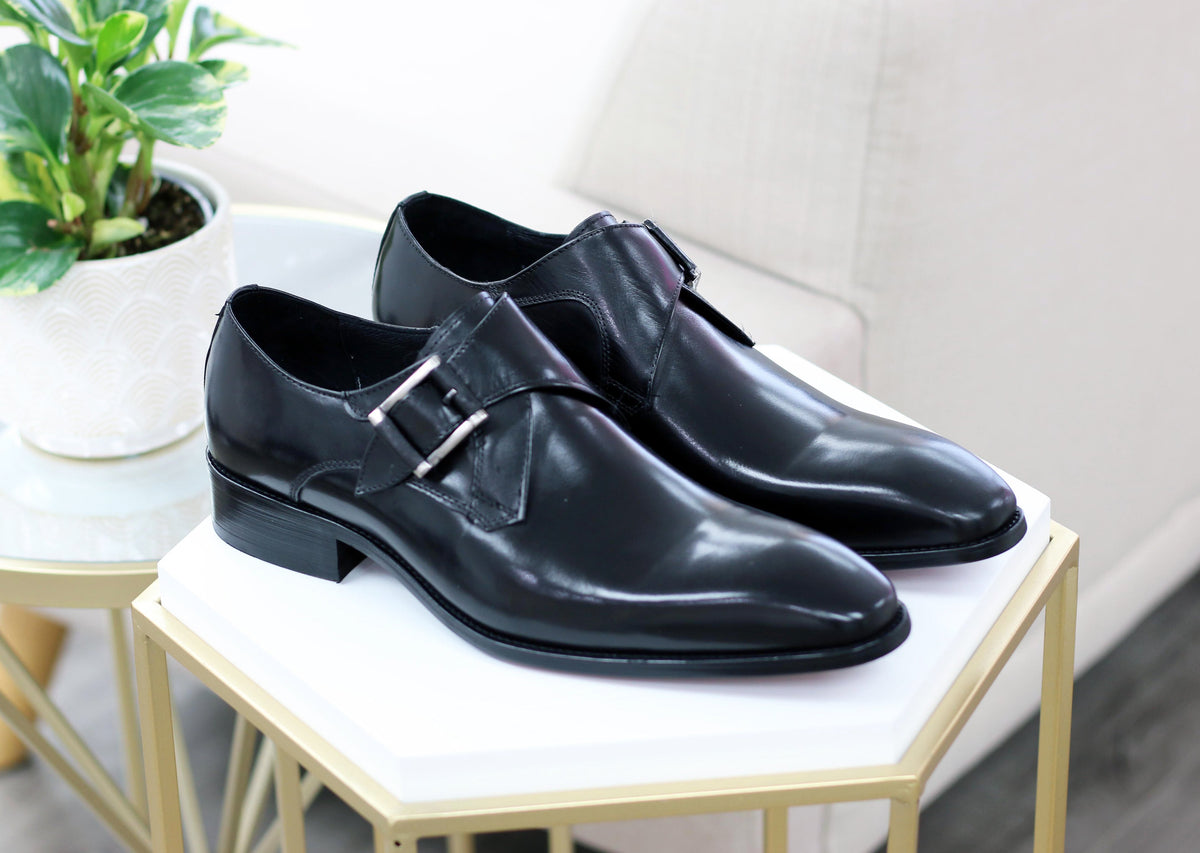 Black monk strap leather dress shoes on a bench, front pair view
