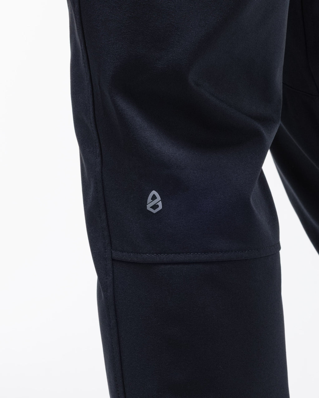 Black chino pants hem close-up with small logo patch on the side seam.