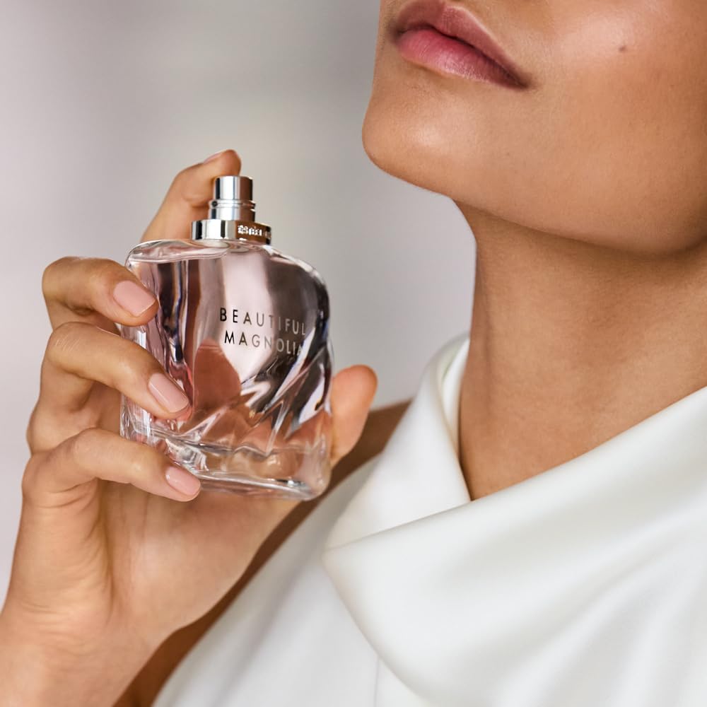 Eau de parfum bottle in clear pink glass with silver spray cap held near face