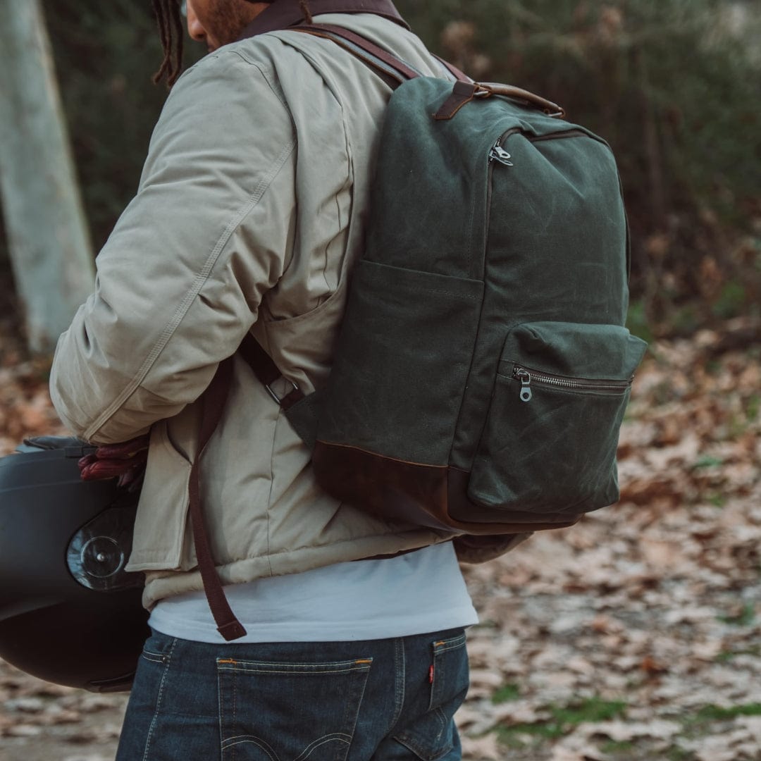 Green canvas backpack on person’s back with top handle and front zip pocket.