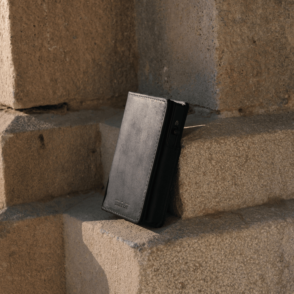 Gray bifold wallet with dark side panel and card slots, standing against bricks.