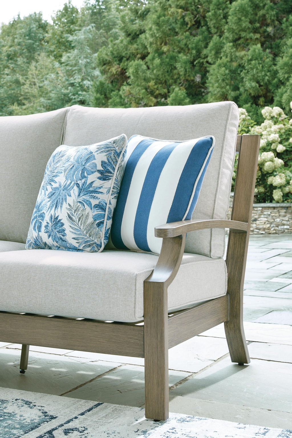 Outdoor sofa loveseat with light gray seat and two blue floral striped accent pillows