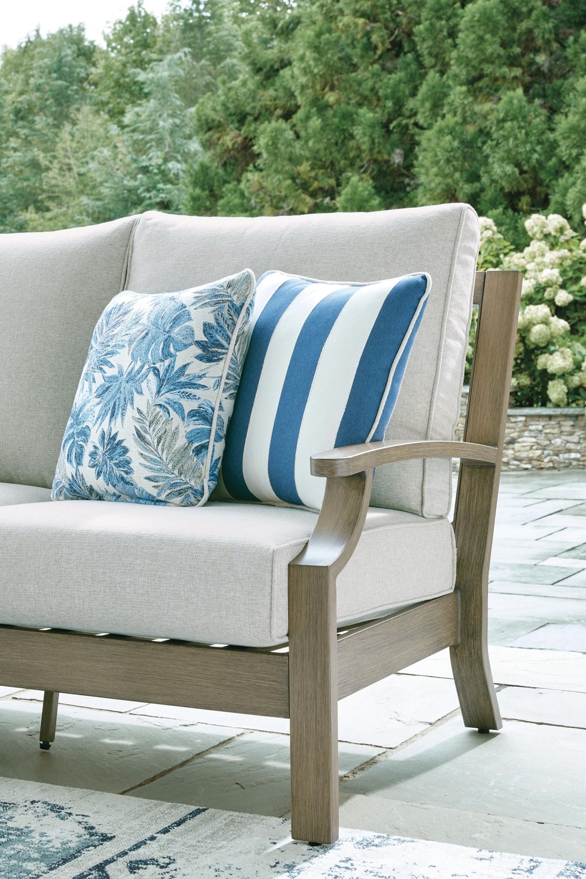 Outdoor sofa loveseat with light gray seat and two blue floral striped accent pillows