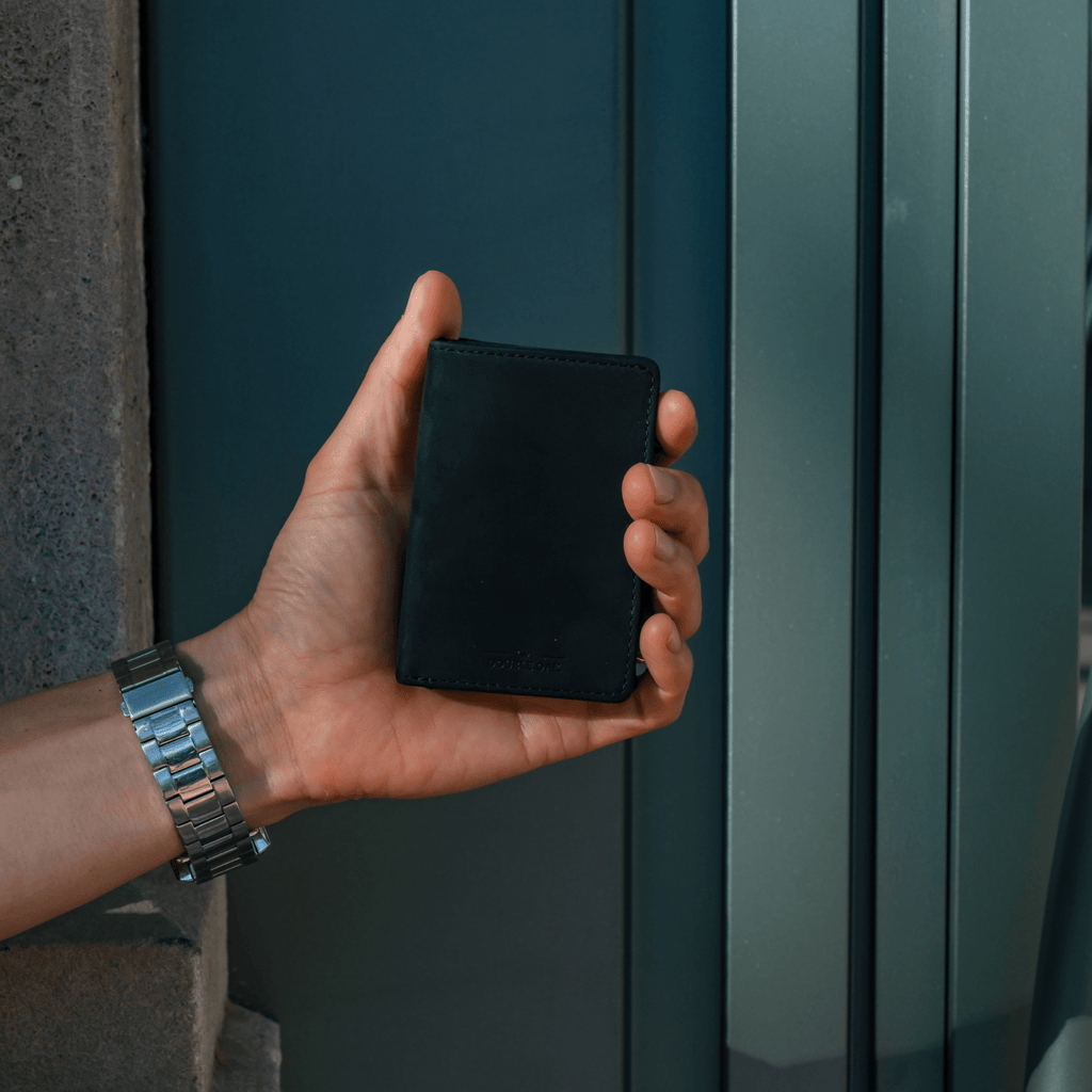 Dark teal bifold wallet with stitched edges, held against a building.