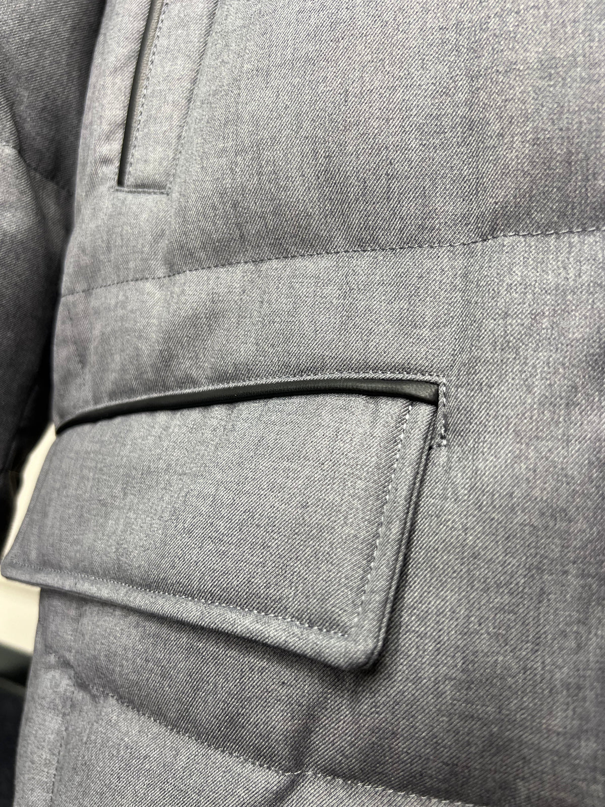 Grey padded coat sleeve with buttoned pocket flap and stitched border