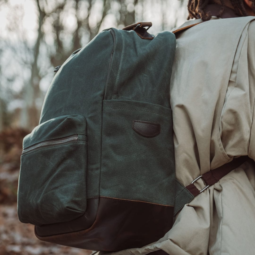 Dark green backpack with top handle straps and front zip pocket; brown base panel.