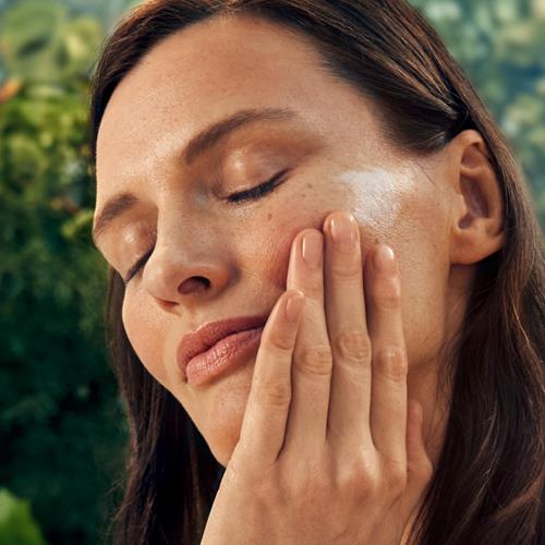 Woman applying moisturizer with hands to cheek and around eye