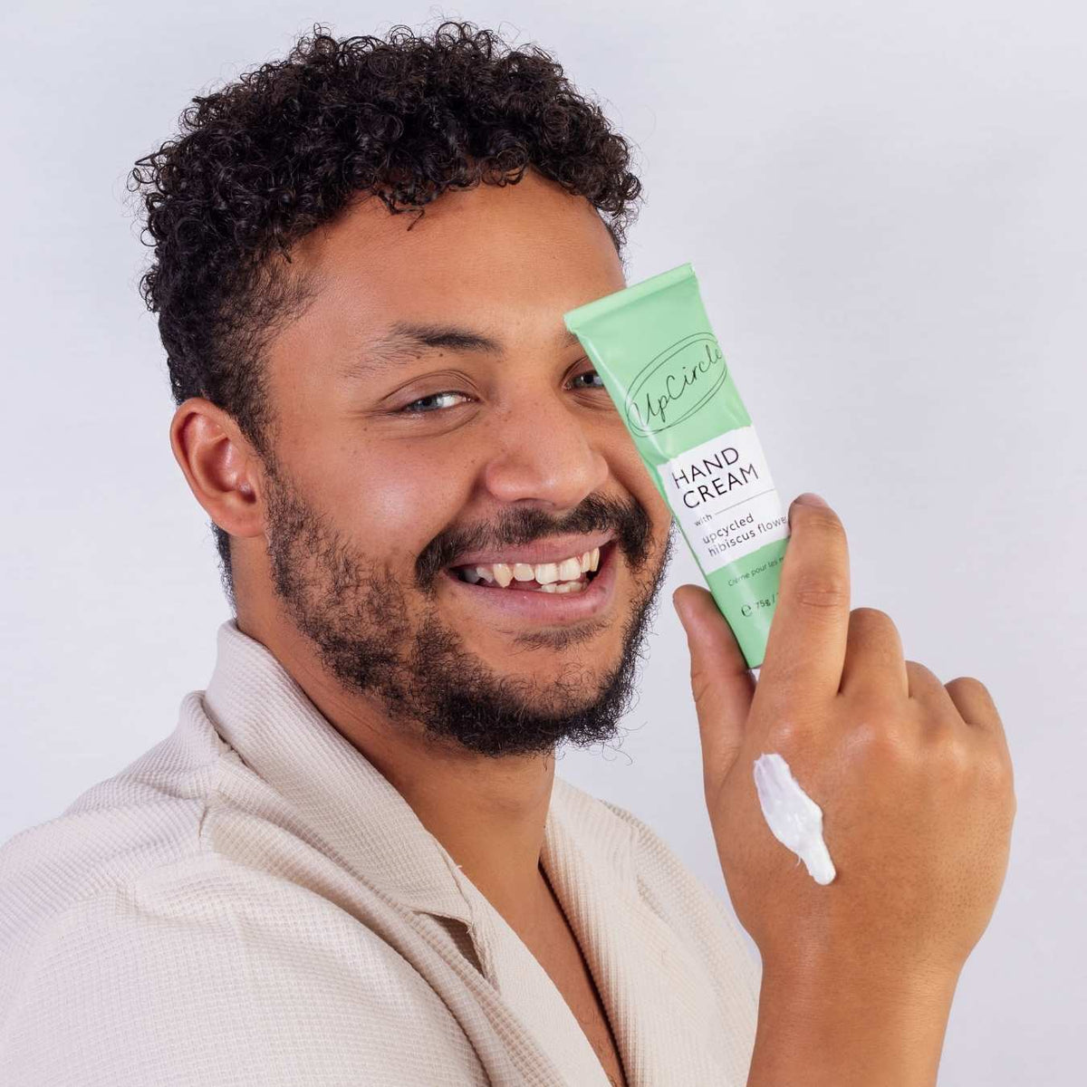 UpCircle green hand cream tube held by a man, cream on fingertip