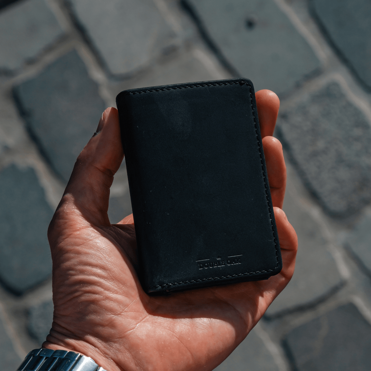Black bifold wallet with logo at bottom, stitched leather front.