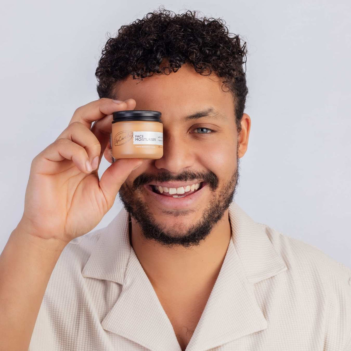 Man holding a small face moisturizer jar near his cheek