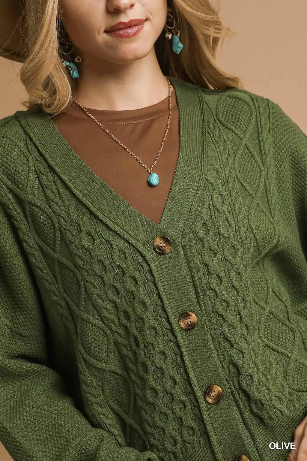 Olive cable-knit V-neck cardigan close-up with wood-look buttons and turquoise necklace.