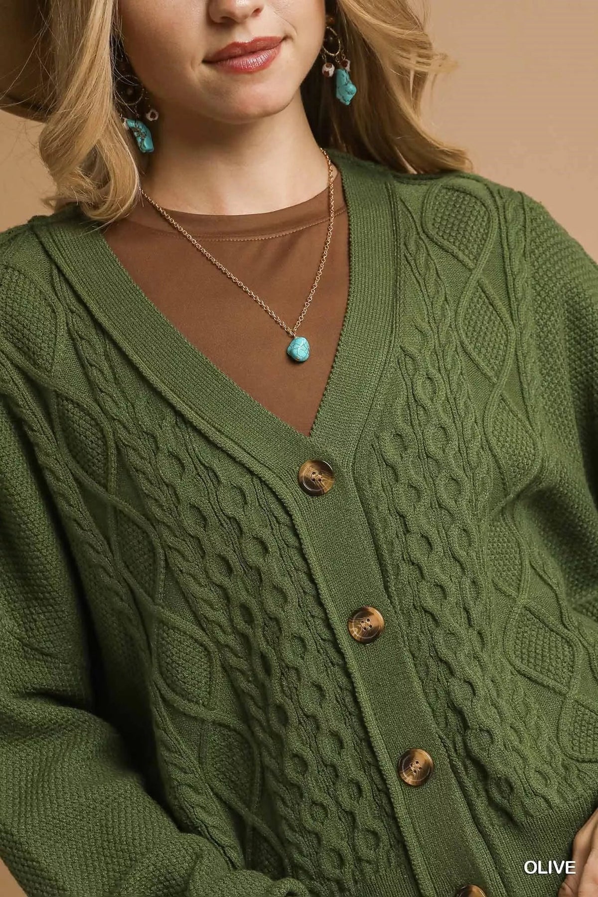 Olive cable-knit V-neck cardigan close-up with wood-look buttons and turquoise necklace.