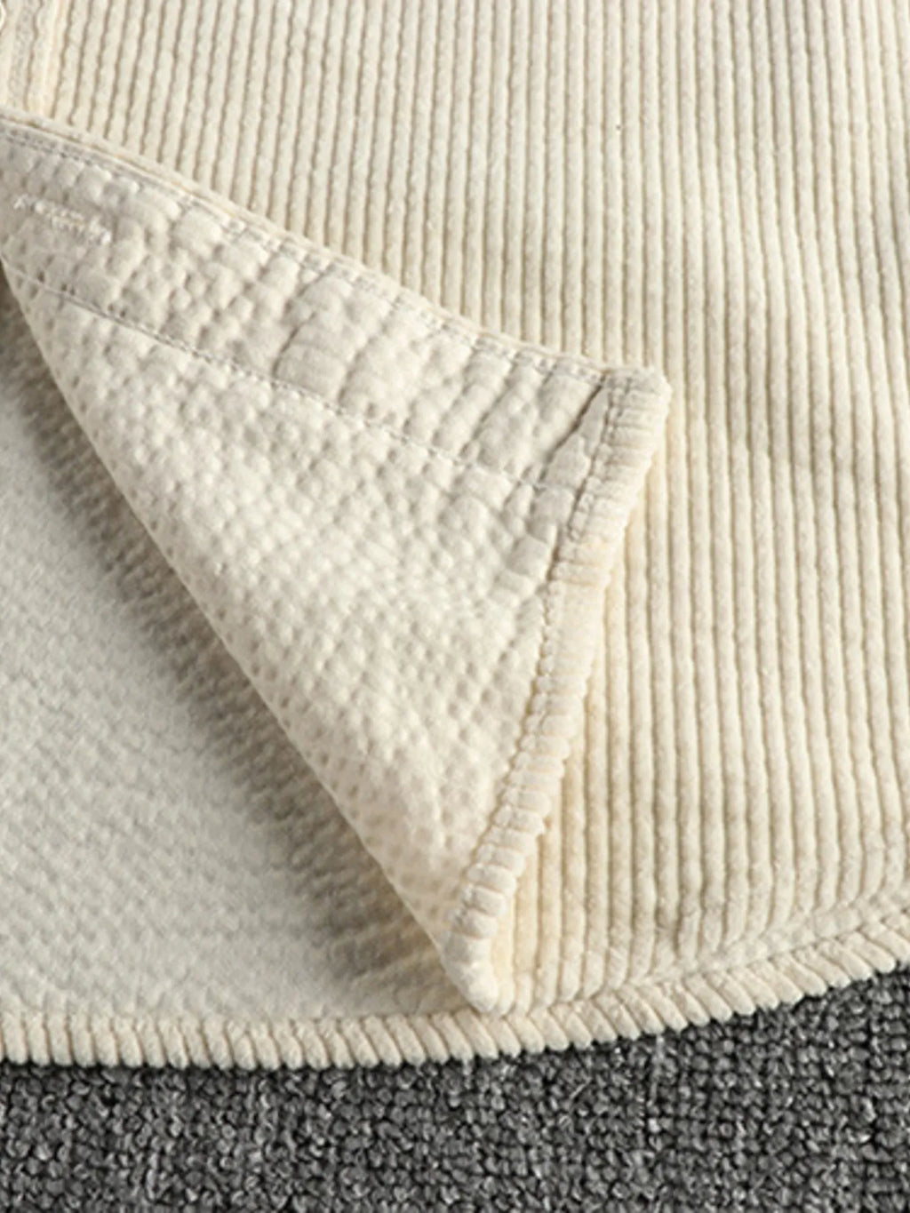 Close-up of light beige corduroy shirt hem and side seam with curved pocket opening