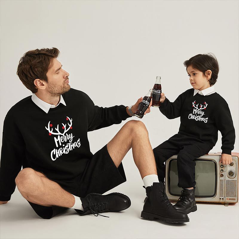 Black Christmas sweaters with reindeer 'Merry Christmas' print, worn by adults and child.