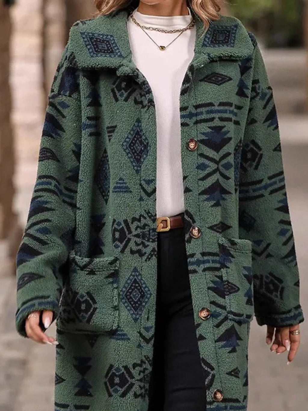Geometric longline button-up coat in green with large patterned motifs, button placket visible.