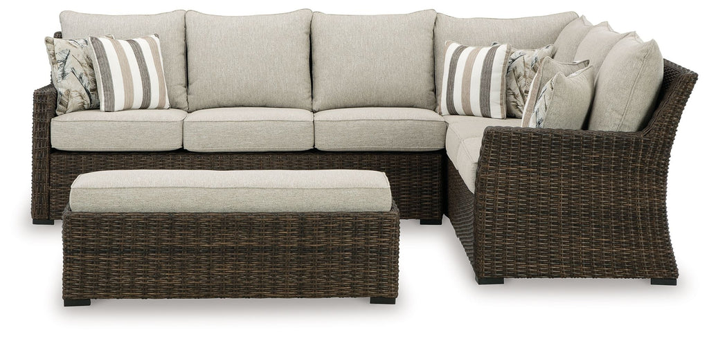 Sectional sofa with brown wicker arms, light beige seat cushions and striped throw pillows