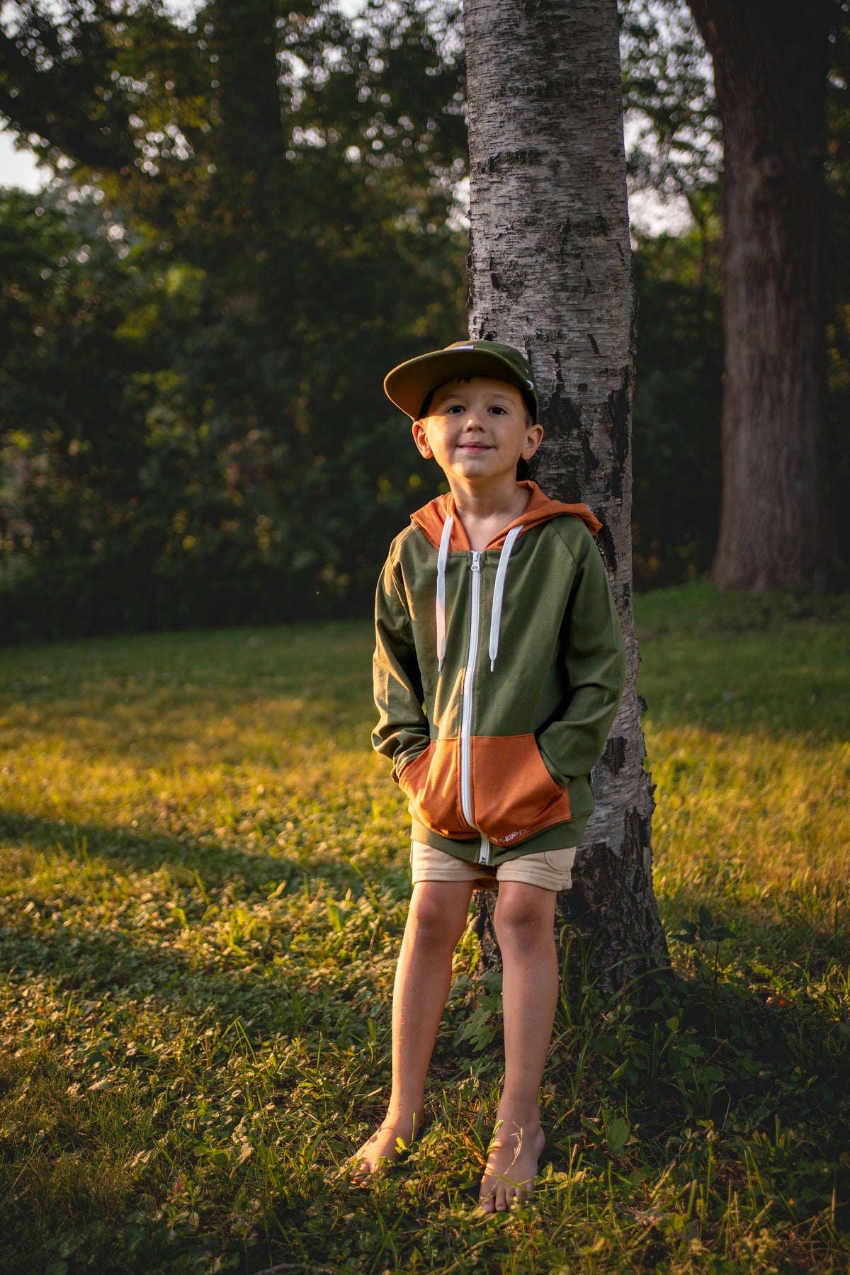 Kids green zip hoodie with orange hood and white drawcords, worn outdoors